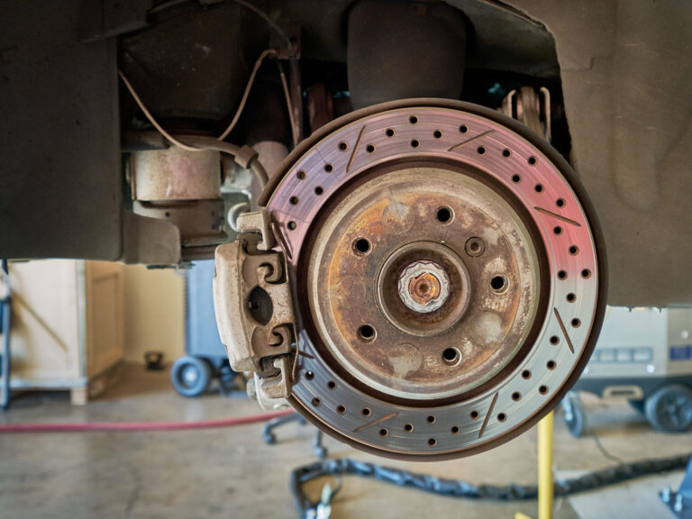 rusty slotted and drilled brake rotor with caliper assembly before cleaning