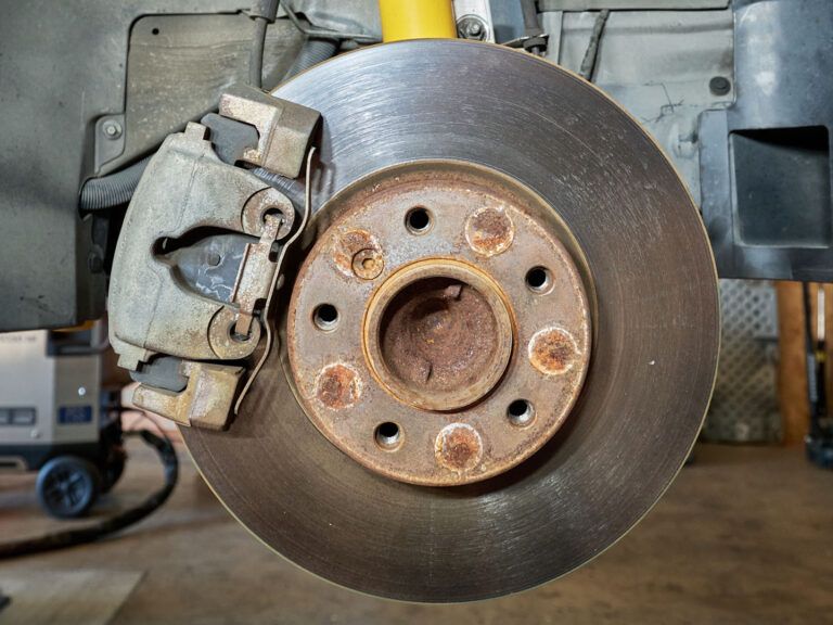 close-up of a car brake rotor and caliper showing rust and dirt buildup before cleaning