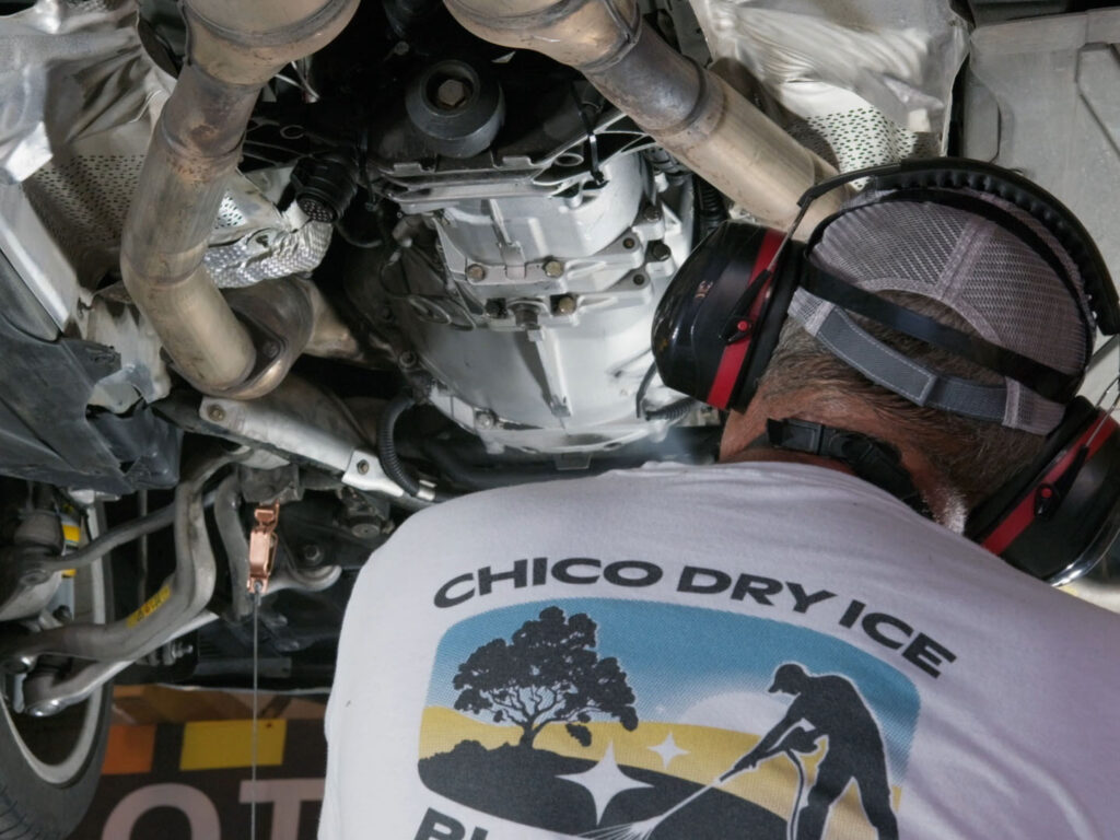 Chico Dry Ice Blasting technician working underneath a vehicle wearing protective headphones and branded shirt