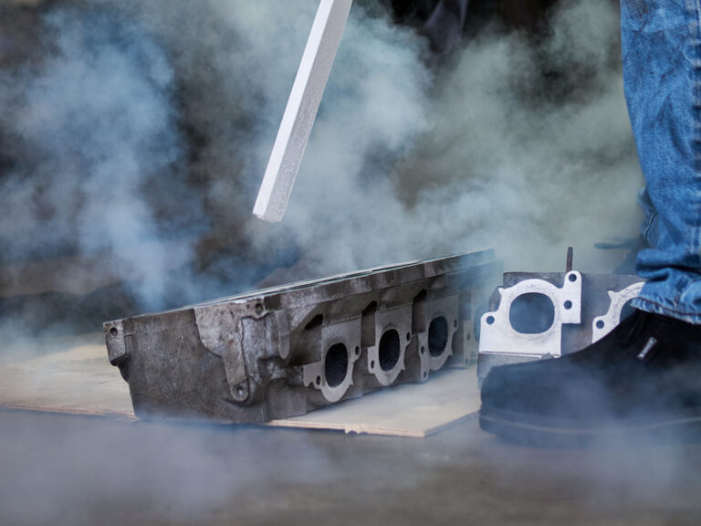 dry ice blasting a metal engine part, surrounded by vapor and technician's foot visible nearby